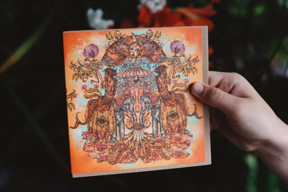 Hand holding a card with intricate design of elephants and floral elements against a dark background
