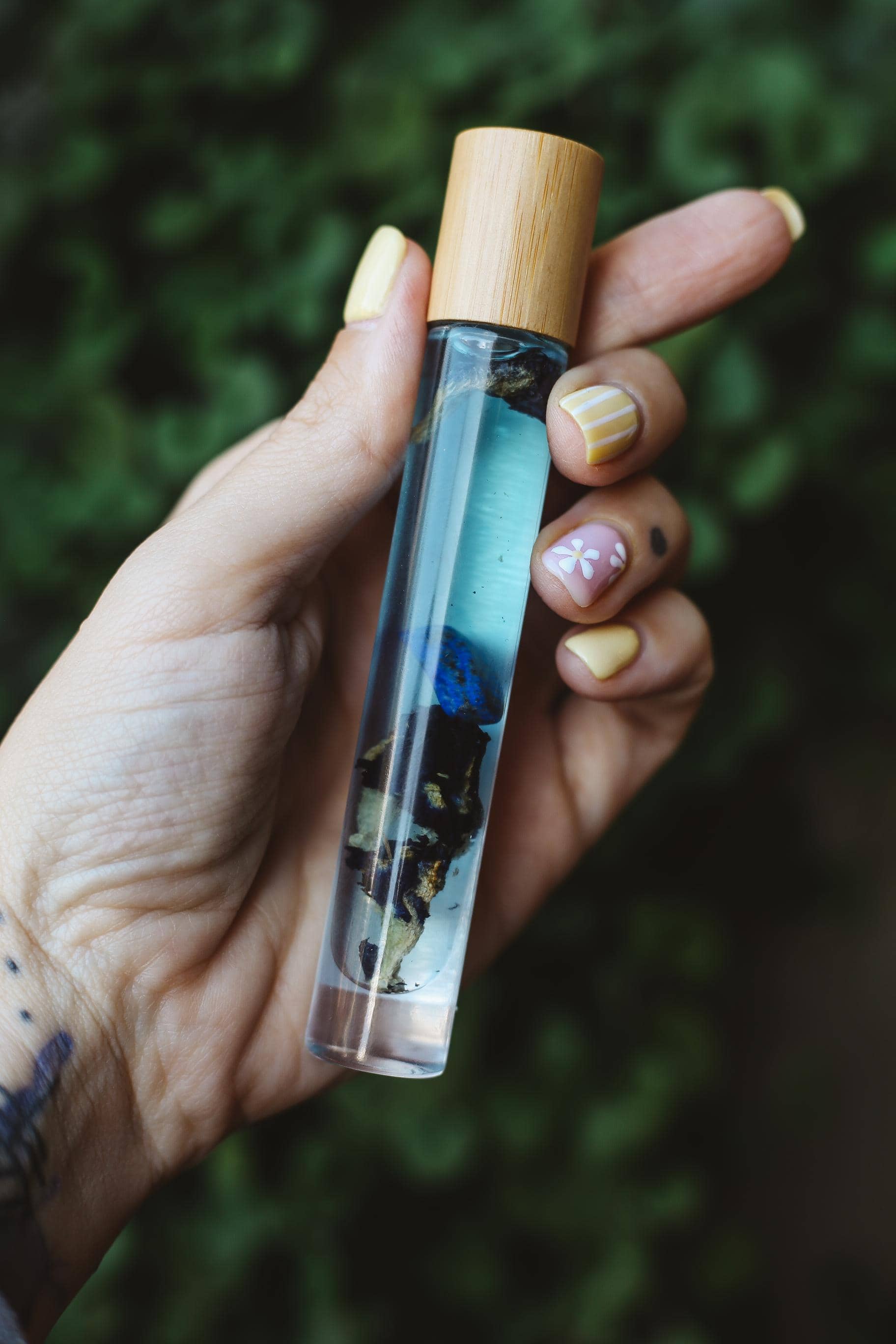 Hand holding a small glass bottle with a wooden cap against a blurred green background