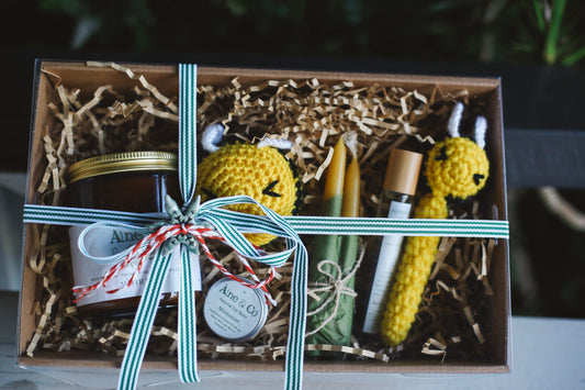 Gift box with decorative items including a glass jar artisan candle, crochet toys, and beeswax candles, natural lip balm and hedgerow oil