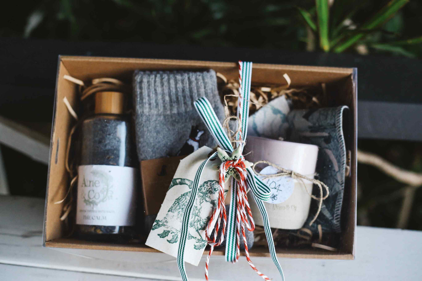 Gift set with a candle, socks, and other items in a box with decorative ribbons.