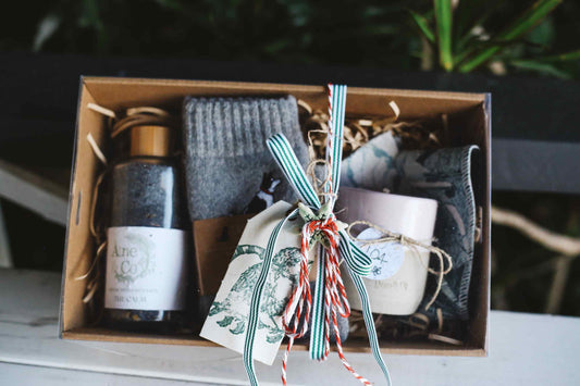 Gift set with a candle, socks, and other items in a box with decorative ribbons.