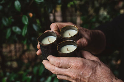 Hands holding three of Àine & Co. Beard and Face Balm Candle with cotton wick in ceramic milk jug 