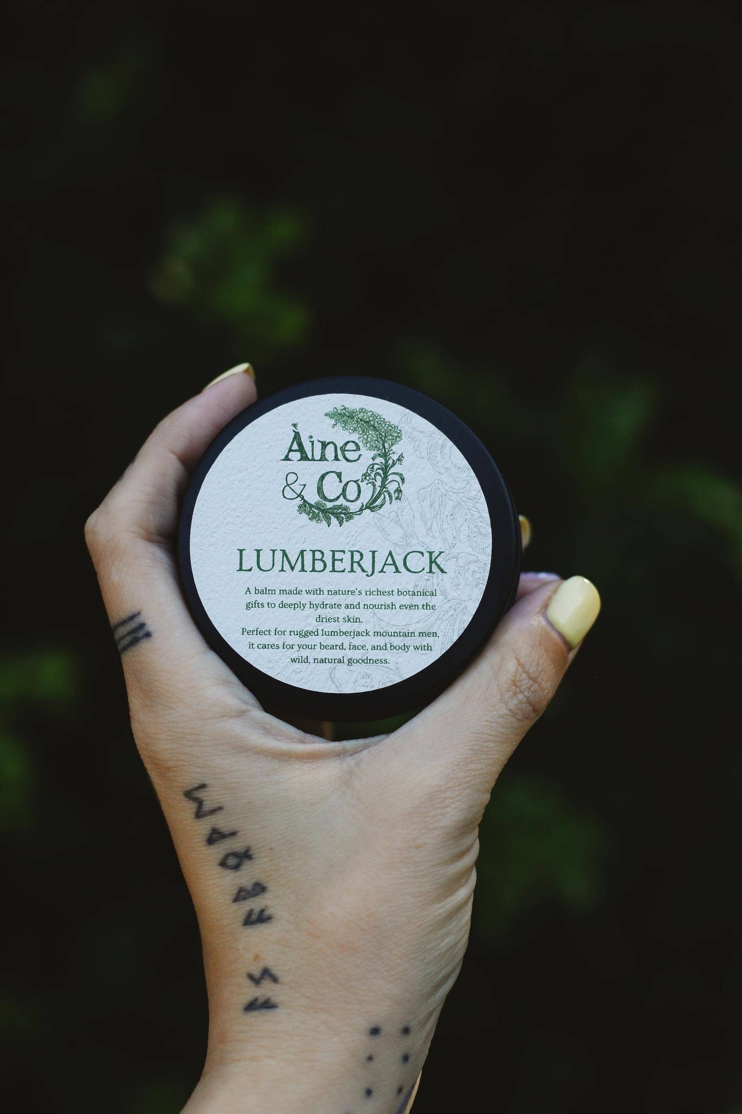 Hand holding a container labeled 'Aine & Co Lumberjack' against a dark background