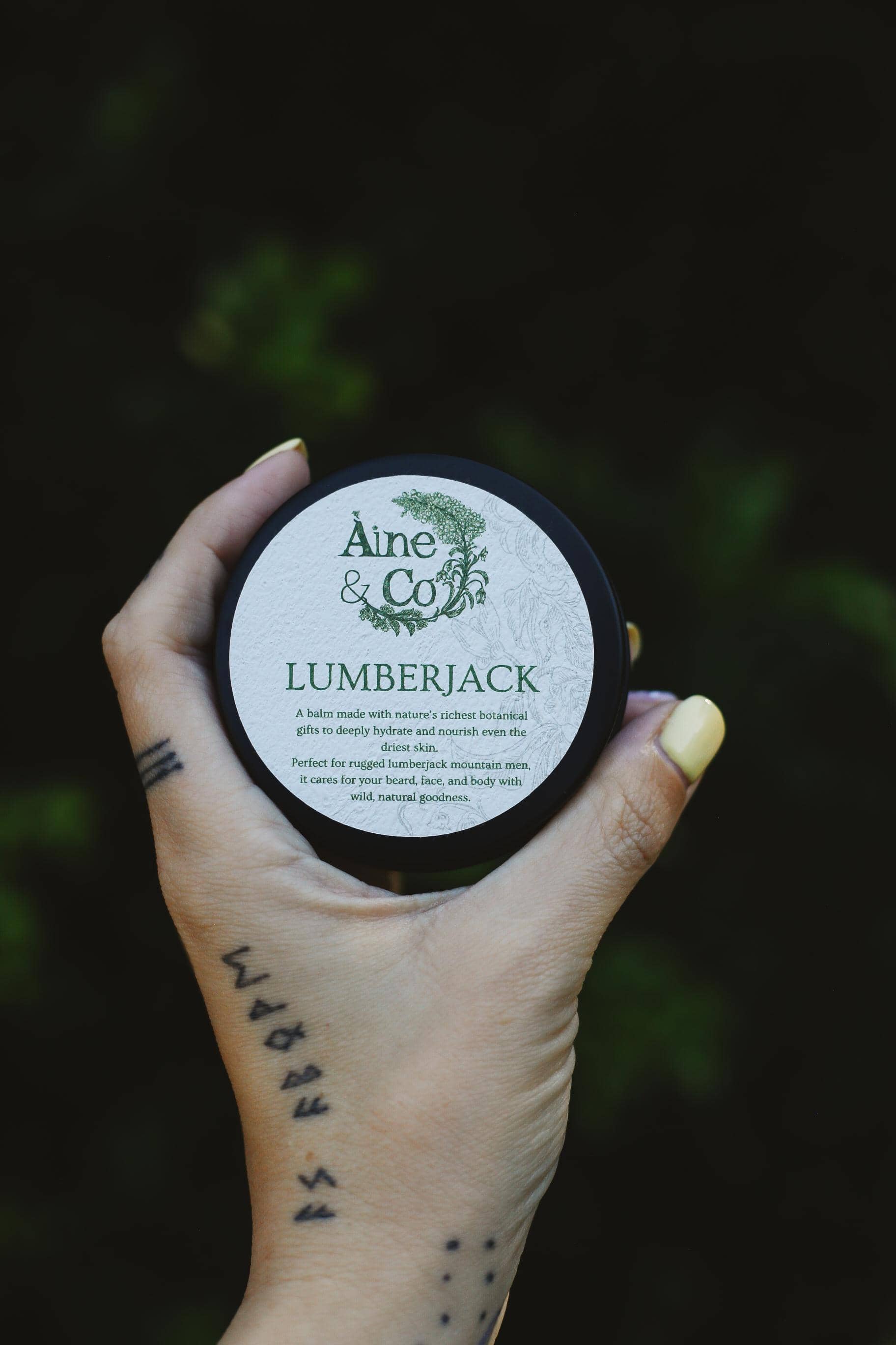 Hand holding a container labeled 'Aine & Co Lumberjack' against a dark background