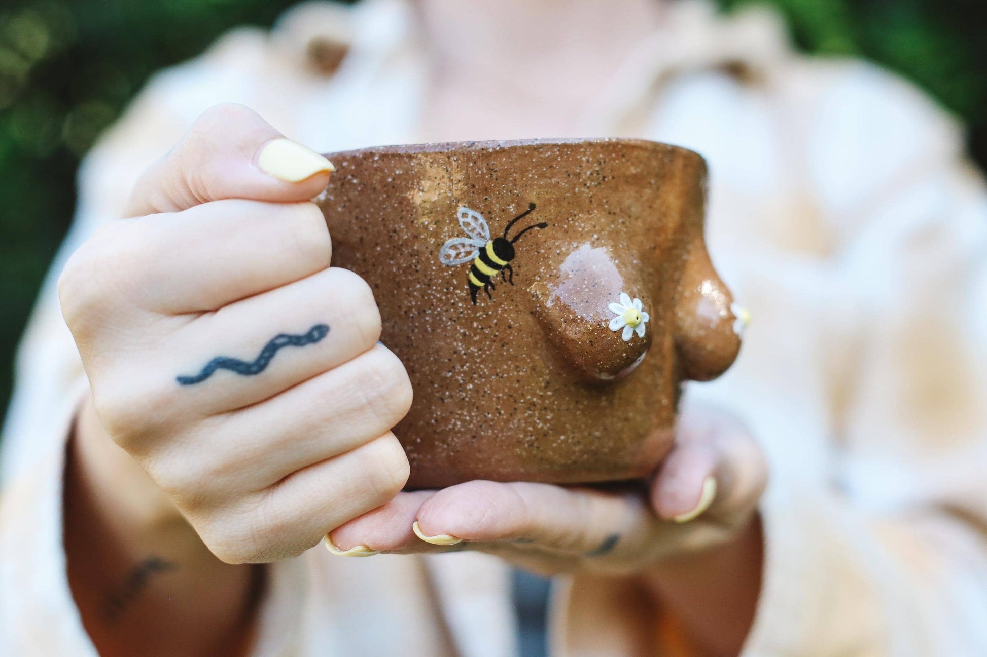 Person holding a brown ceramic mug with a bee design, blurred background