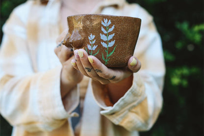 Person holding a ceramic mug with breast shapes and plant designs 