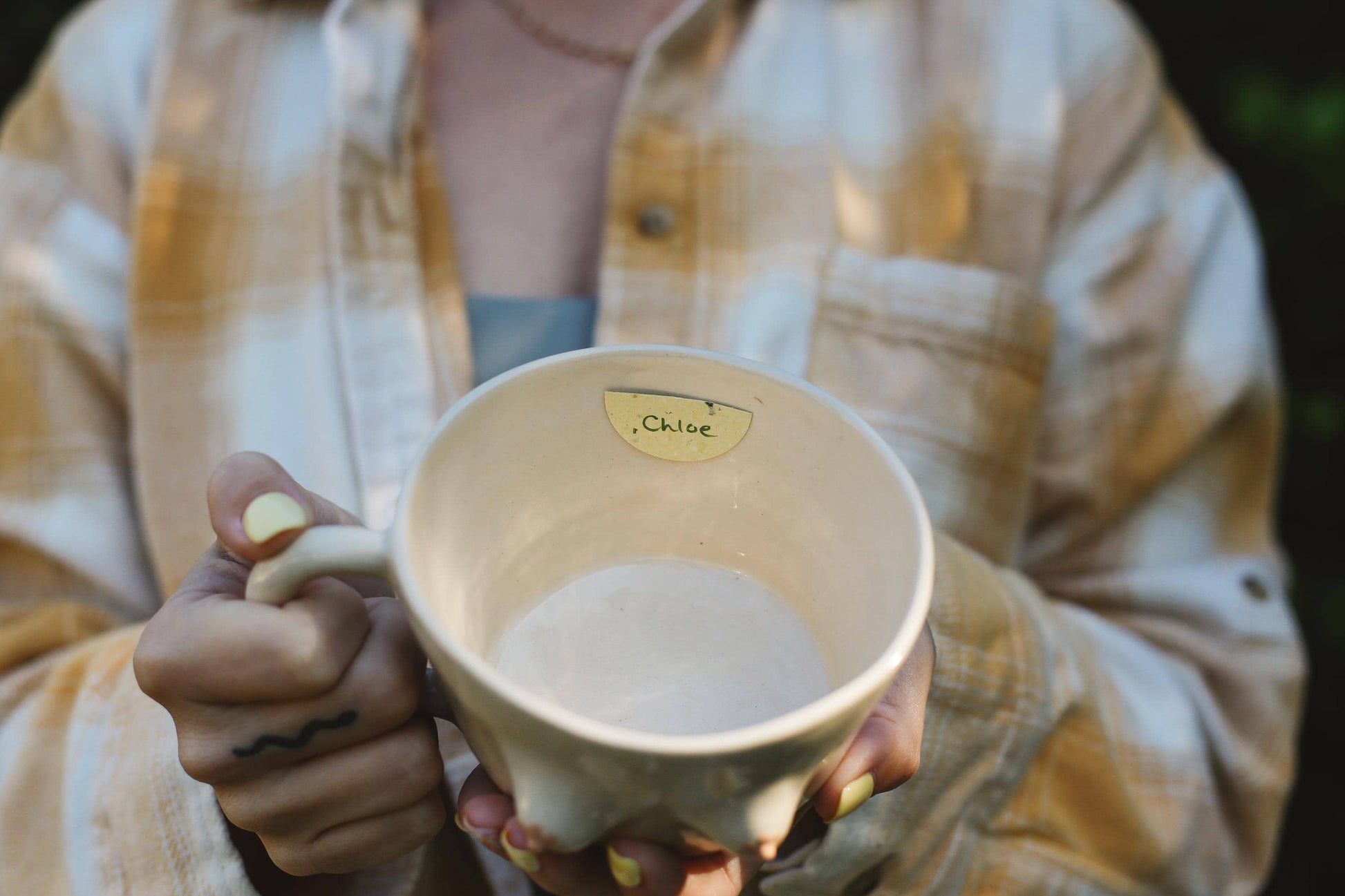 Person holding a ceramic mug with a name tag "Chloe".