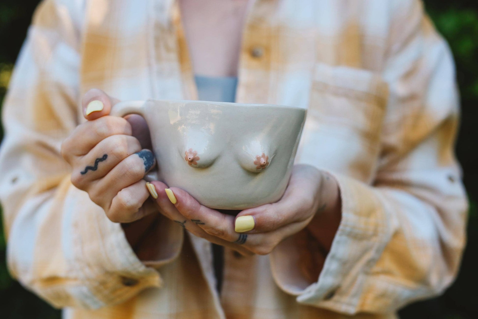 Person holding a ceramic cup with breast-like designs outdoors