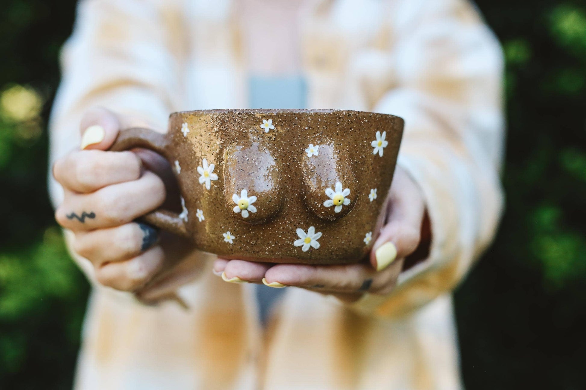 Person holding a brown mug with floral patterns outdoors