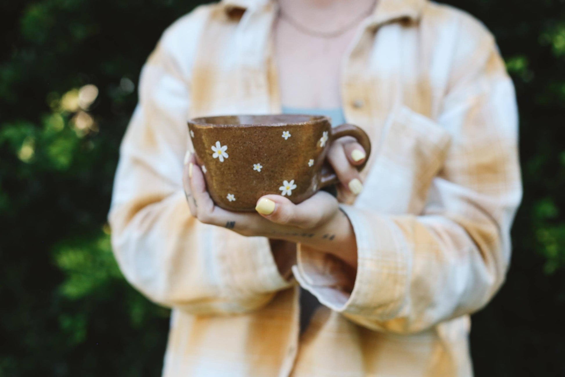 Person holding a brown mug with white floral patterns against a blurred green background