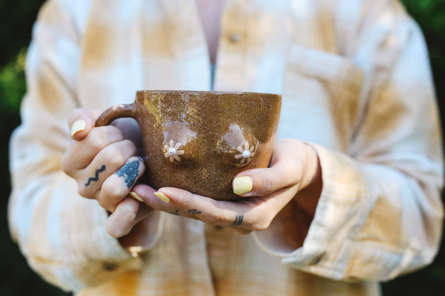 Person holding a brown ceramic mug with boob design