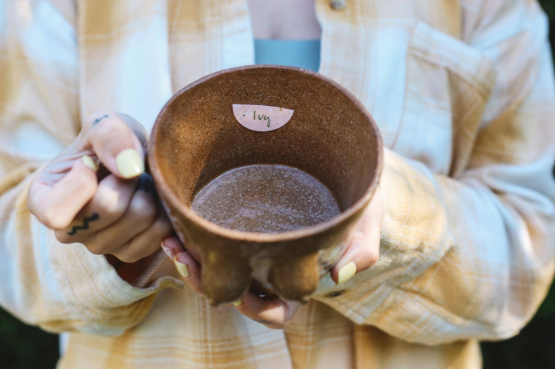 Person holding a brown ceramic mug with a name tag "Ivy"