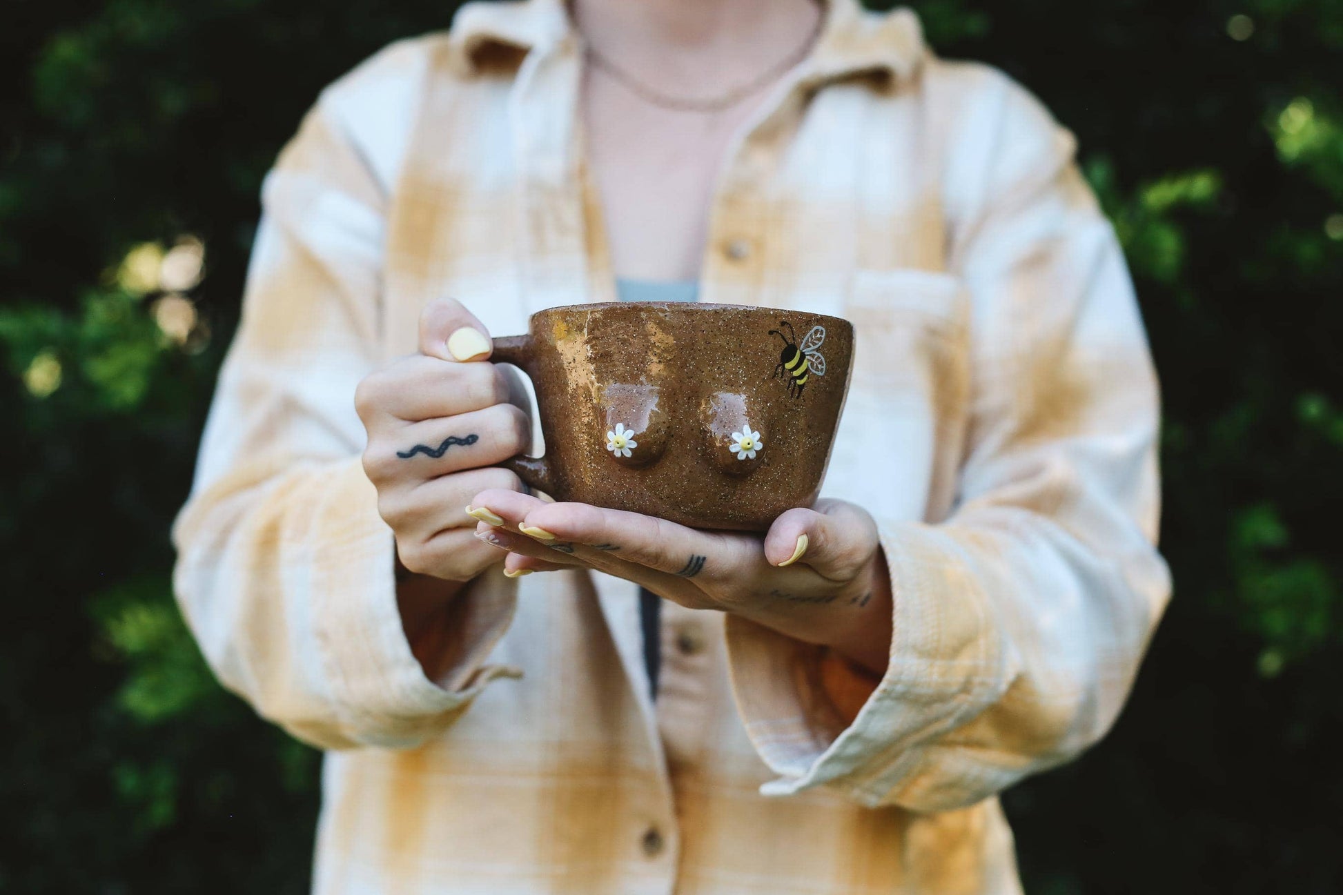Person holding a brown mug with boobs on a blurred green background