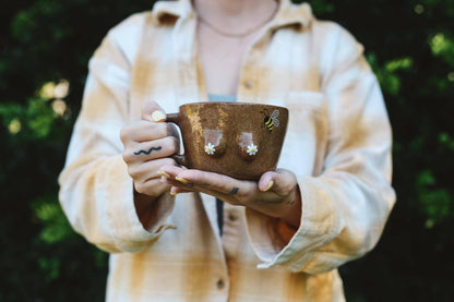 Person holding a brown mug with boobs on a blurred green background