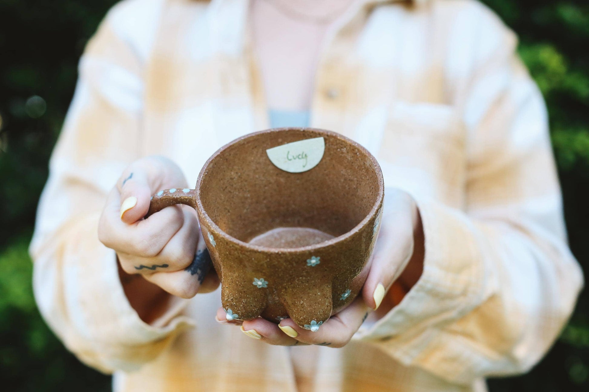 Person holding a brown ceramic mug with a blurred background