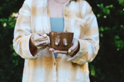 Person holding a brown ceramic cup with a blurred background