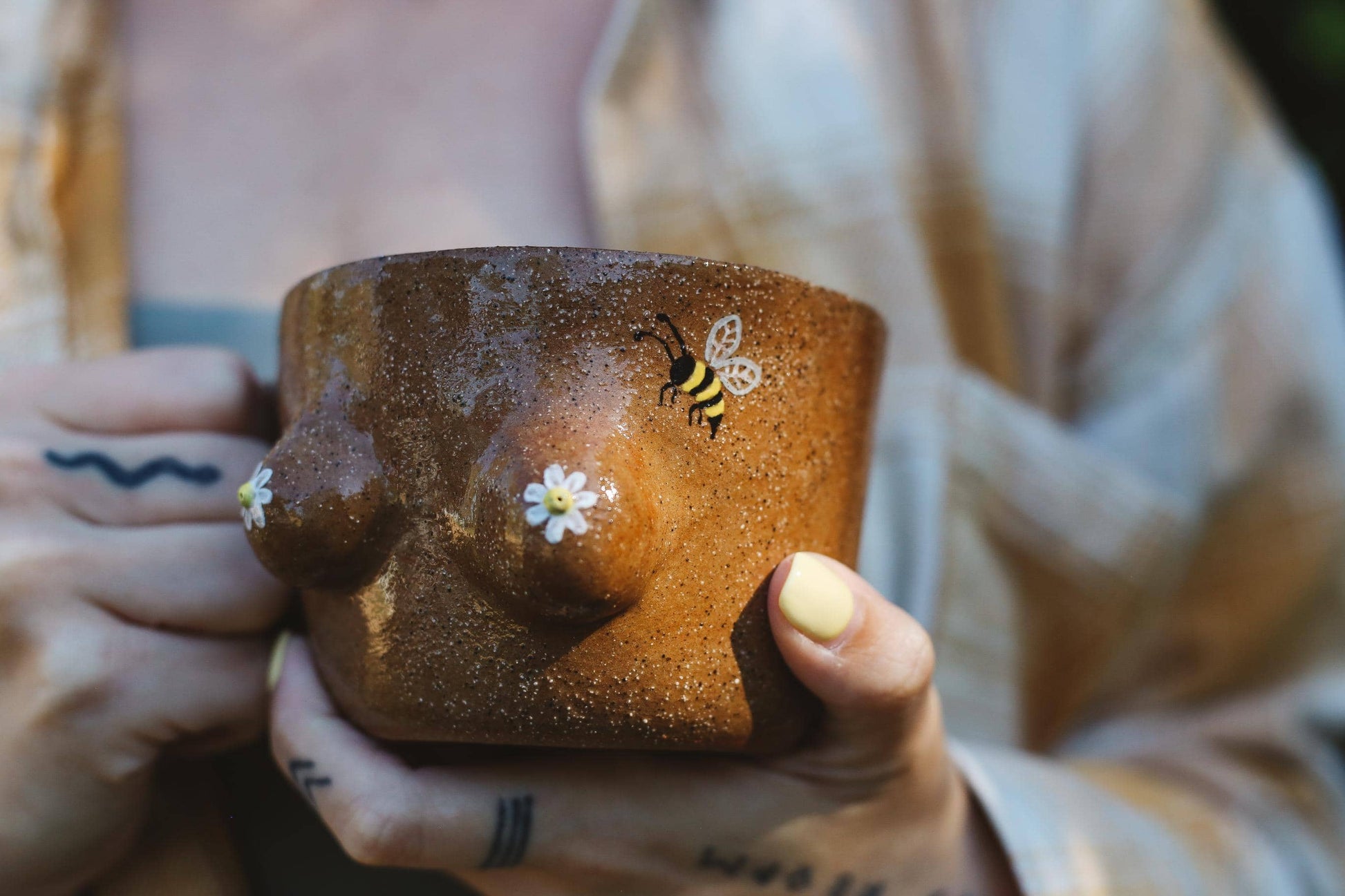 Person holding a brown ceramic mug with a bee and flower design.