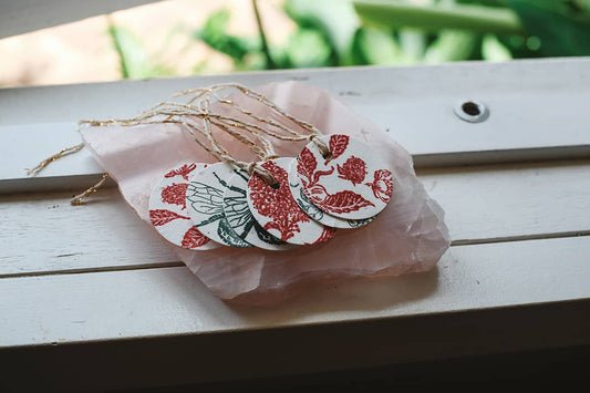 Àine & Co. Hand Stamped Seed Paper Gift Tags in assorted red and green, displayed on rose quartz crystal block