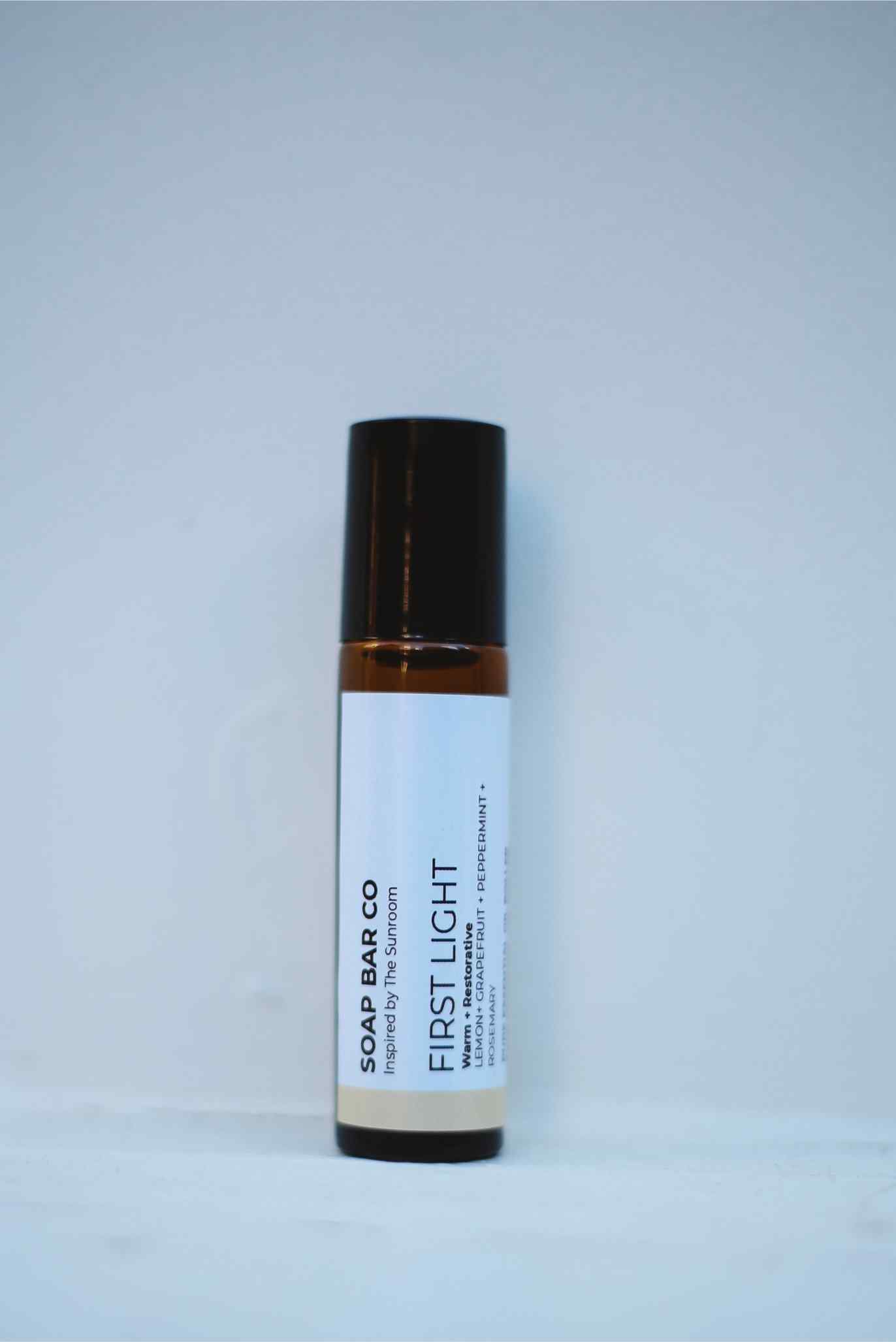 A single roll-on bottle of Soap Bar Co. First Light roll-on deodorant, featuring a white label and a dark brown cap, set against a plain light gray background.