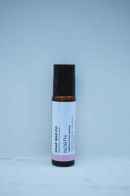 A small amber glass soap bar bottle with a black cap and a white label reading 'SOAP BAR CO NORTH', set against a plain light blue background.