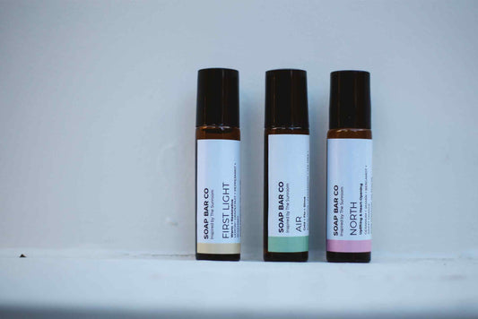 Three small roll-on bottles labeled 'SOAP BAR CO' with scent names FIRSTLIGHT, AIR, and NORTH, standing upright on a white surface against a light gray background.