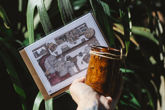 Hand holding a card with a cartoon design against a leafy green background
