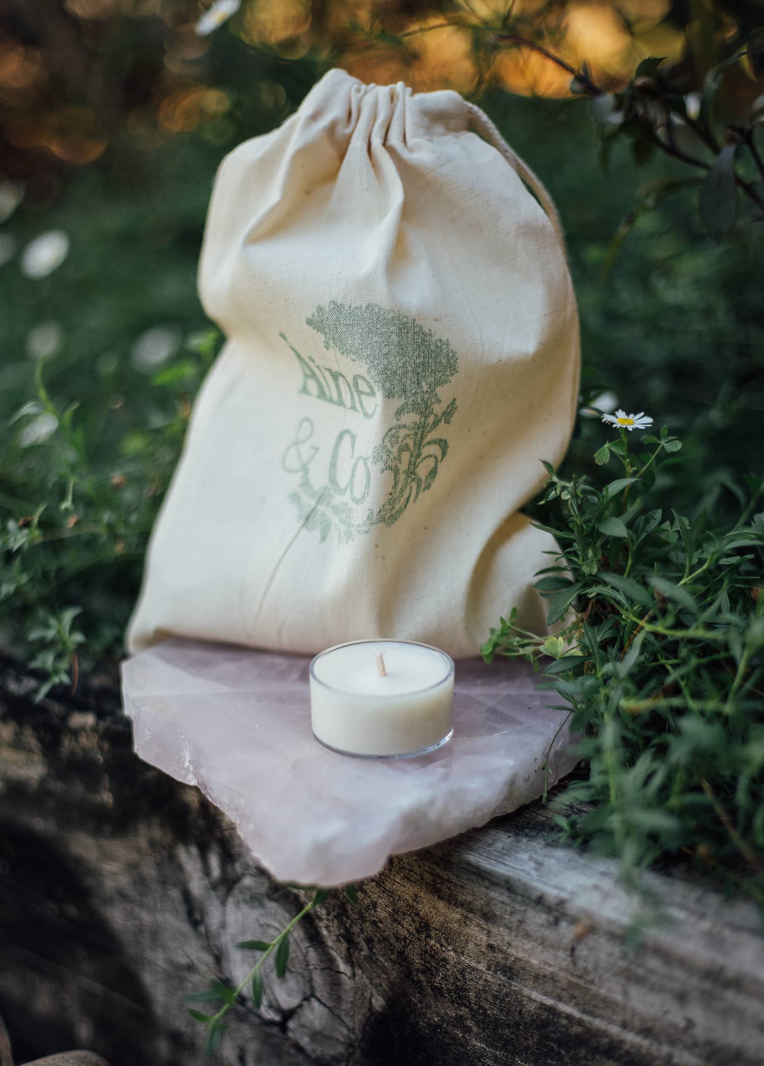 An unlit Àine & Co. Tea Light in size small, shown with the Àine & Co. logo calico drawstring bag