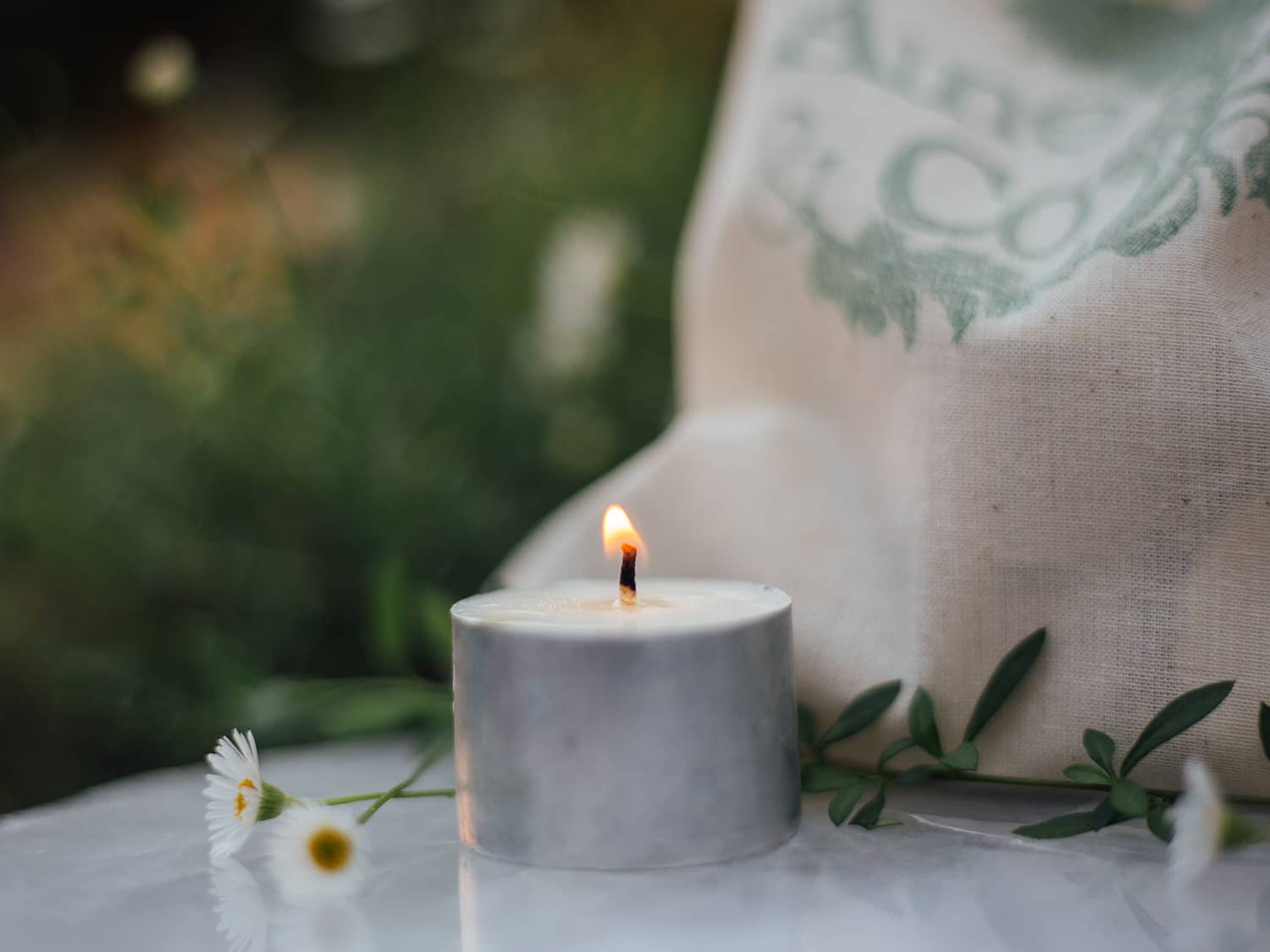 A lit Àine & Co. Tea Light, shown with the Àine & Co. calico drawstring bag