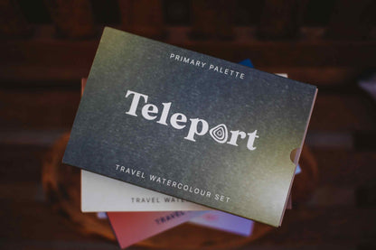 Teleport Primary Palette travel watercolour set, showing the dark textured cover with white text, resting on a stack of other color palettes.