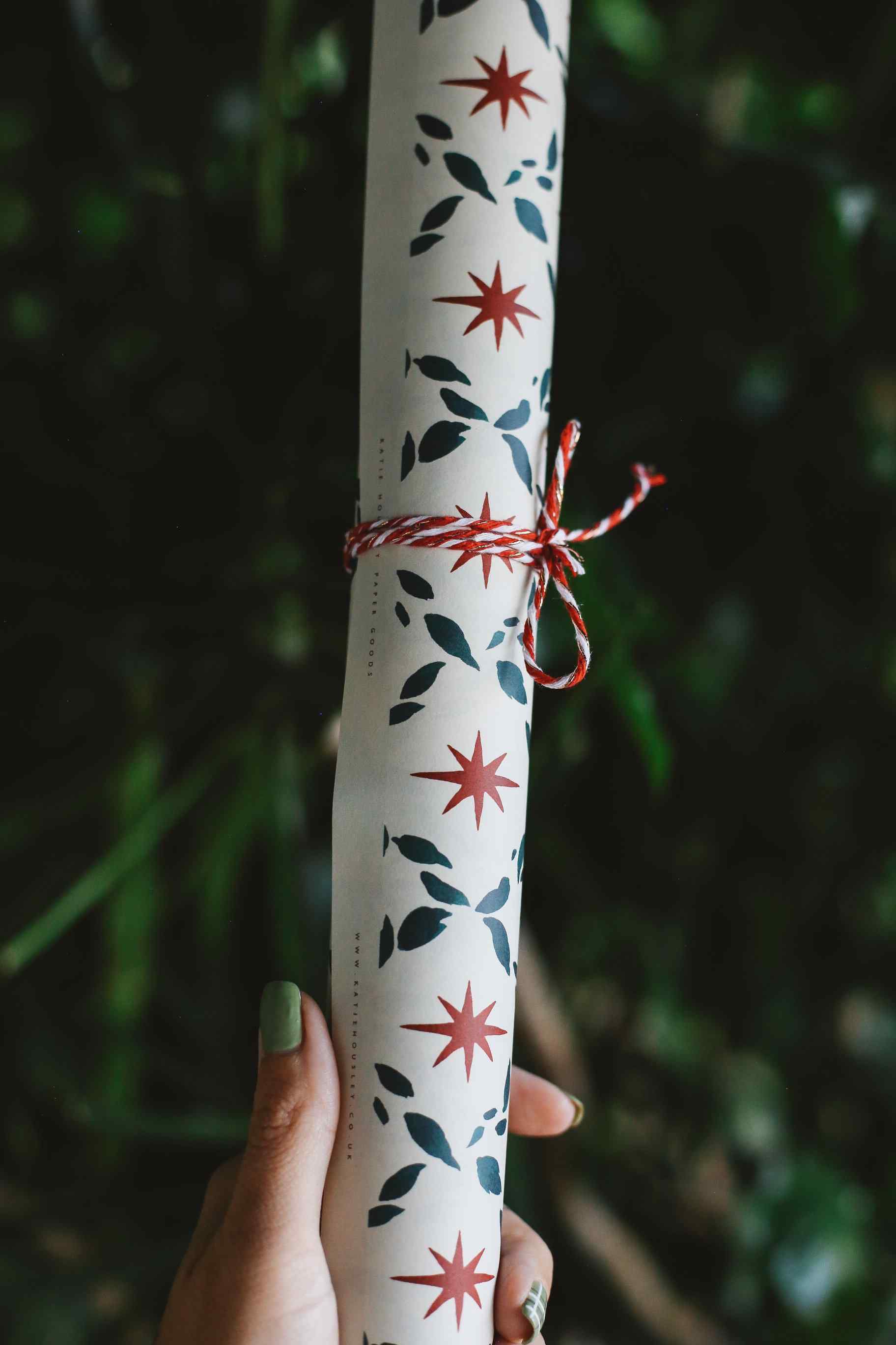 Roll of decorative paper with star and leaf pattern held by a hand against a blurred green background